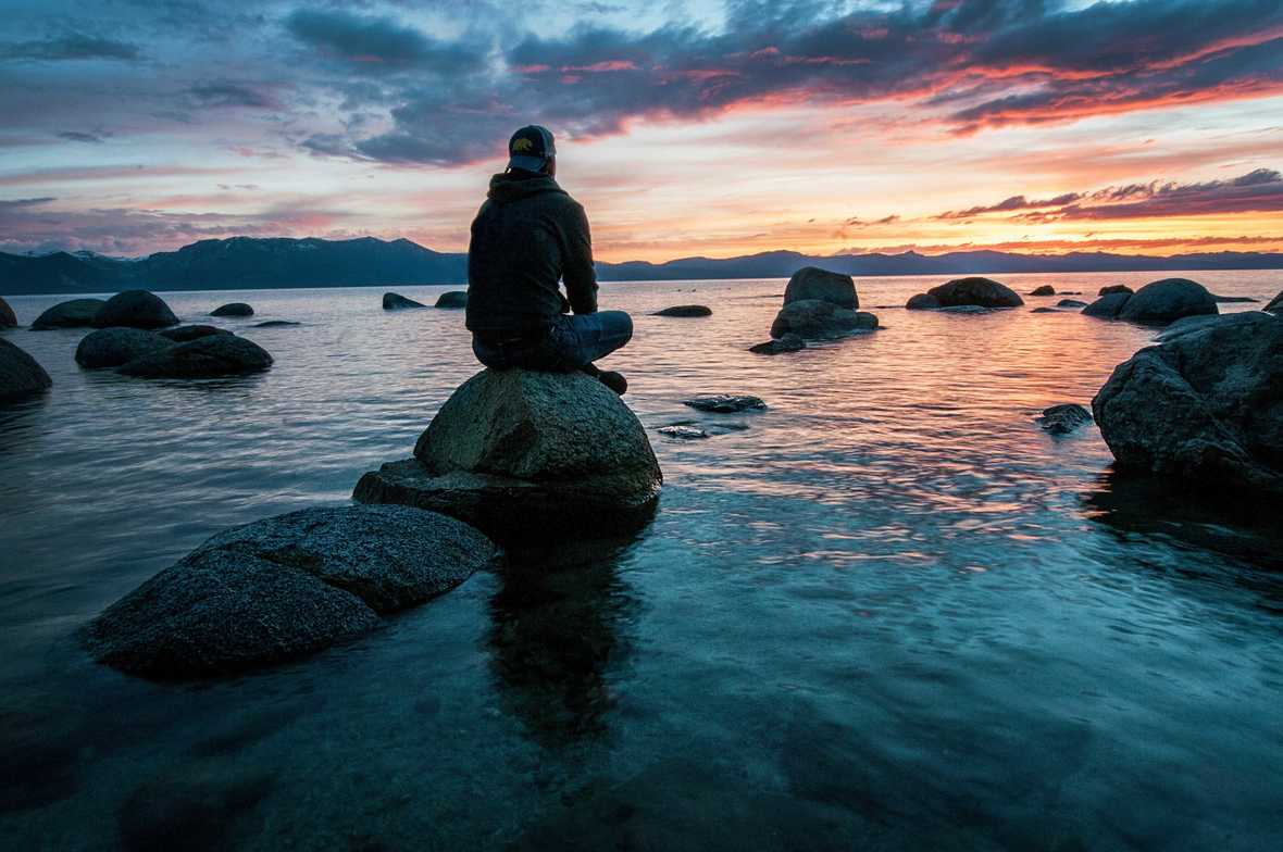 person sitting on a rock in water, sunset in the background